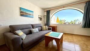 A living room with a grey sofa, a wooden coffee table, a painting of a beach, and a view of the sea through a large window. - Welooveyou Bellatrix Starlight B10 (Costa Calma (incl. Urbanización Cañada del Río))
