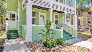 A two-story house with a green exterior and white trim, featuring a front porch with steps and a small garden area. - Cordova Palms - 4BR near Castillo w/ BBQ (St. Augustine)