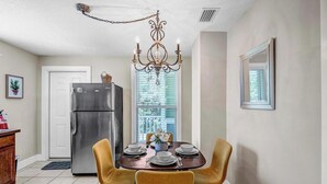 A dining area with a chandelier, a refrigerator, and a dining table set for four. - Cordova Palms - 4BR near Castillo w/ BBQ (St. Augustine)
