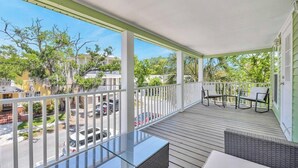 A covered outdoor balcony with a table and chairs, overlooking a street with parked cars and houses. - Cordova Palms - 4BR near Castillo w/ BBQ (St. Augustine)