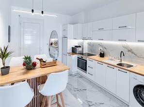 Une cuisine moderne avec des meubles blancs, un plan de travail en bois, un évier, un four à micro-ondes et un lave-linge.