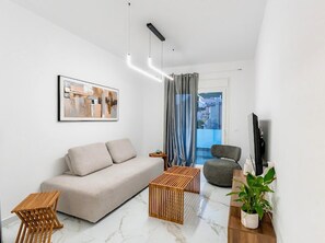 Un salon moderne avec un canapé, une table d’appoint en bois, un fauteuil gris, un téléviseur et une plante en pot.