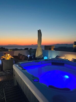 Ein Whirlpool mit blauer Beleuchtung, ein Esstisch mit Kerzen und Blick auf den Sonnenuntergang.
