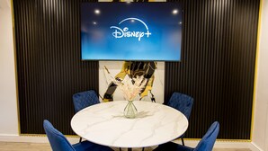 A conference room with a round table, blue chairs, a floral centerpiece, and a Disney+ logo on a screen. - EXCLUSIVE MODERN NEWLY REFURBISHED HOME / CENTRAL LOCATION (Stoke-on-Trent)