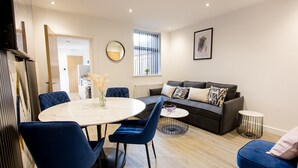 A modern living room with a round dining table, blue chairs, a grey sofa with patterned cushions, and a small round coffee table. - EXCLUSIVE MODERN NEWLY REFURBISHED HOME / CENTRAL LOCATION (Stoke-on-Trent)