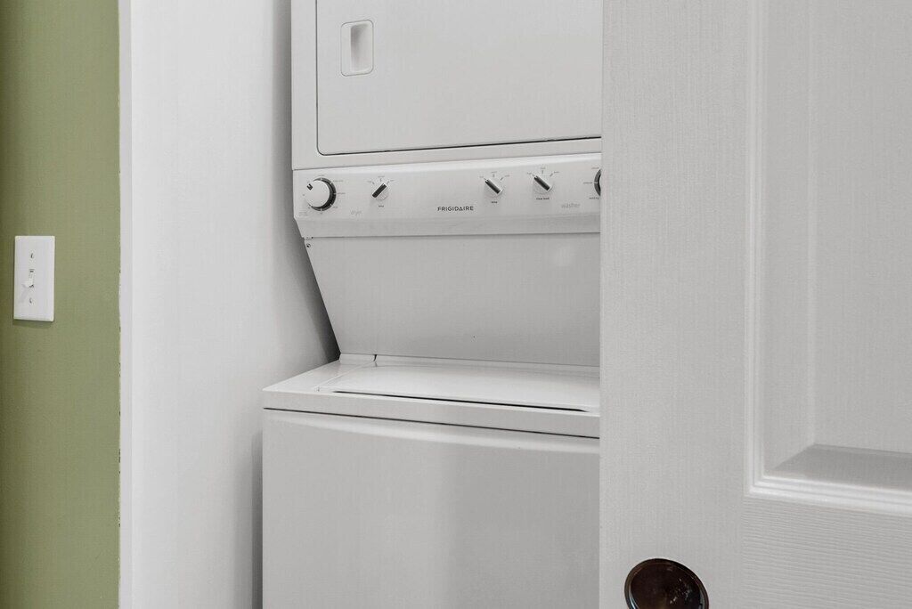 Una lavadora blanca en una habitación con pared verde y una puerta cerrada.