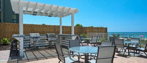 An outdoor patio with a grill, seating area, and a view of the ocean.