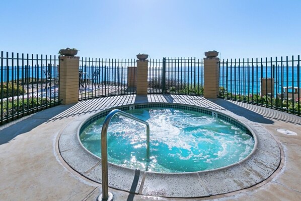 A hot tub with a view of the sea, surrounded by a fence and outdoor seating.