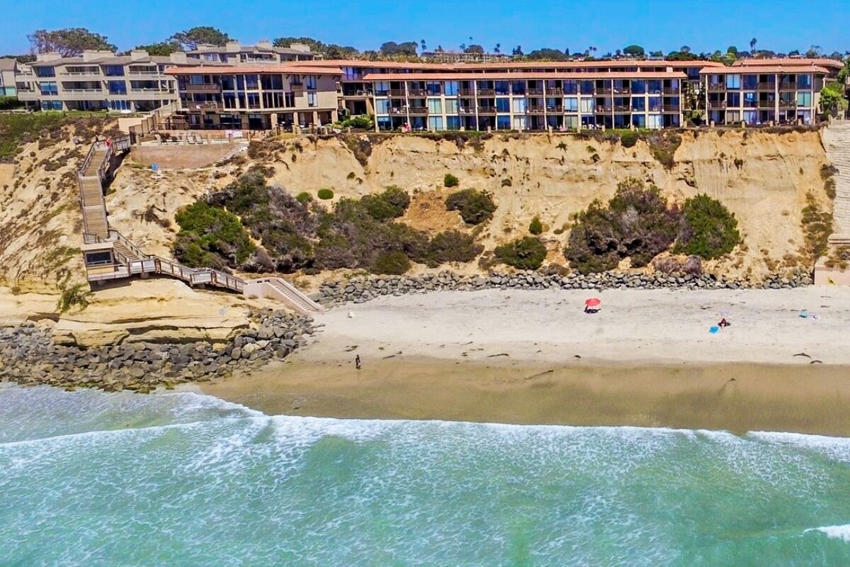 Un hôtel situé sur la côte, avec une falaise rocheuse, une plage de sable et une vue dégagée sur l’océan.