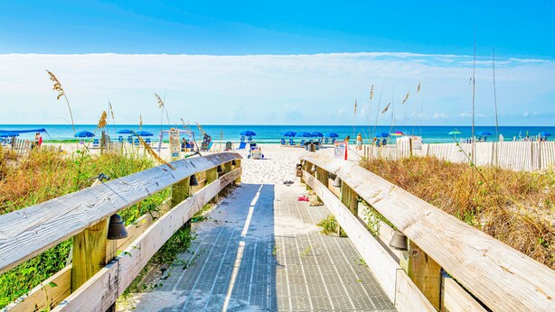 A wooden boardwalk leading to a beach with umbrellas and people.