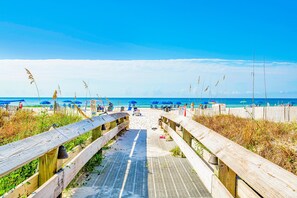 Une promenade en bois menant à une plage où l’on trouve des parasols et des gens.