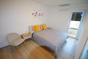 Ein Schlafzimmer mit Bett, Stuhl, Nachttisch und Wandbild.
