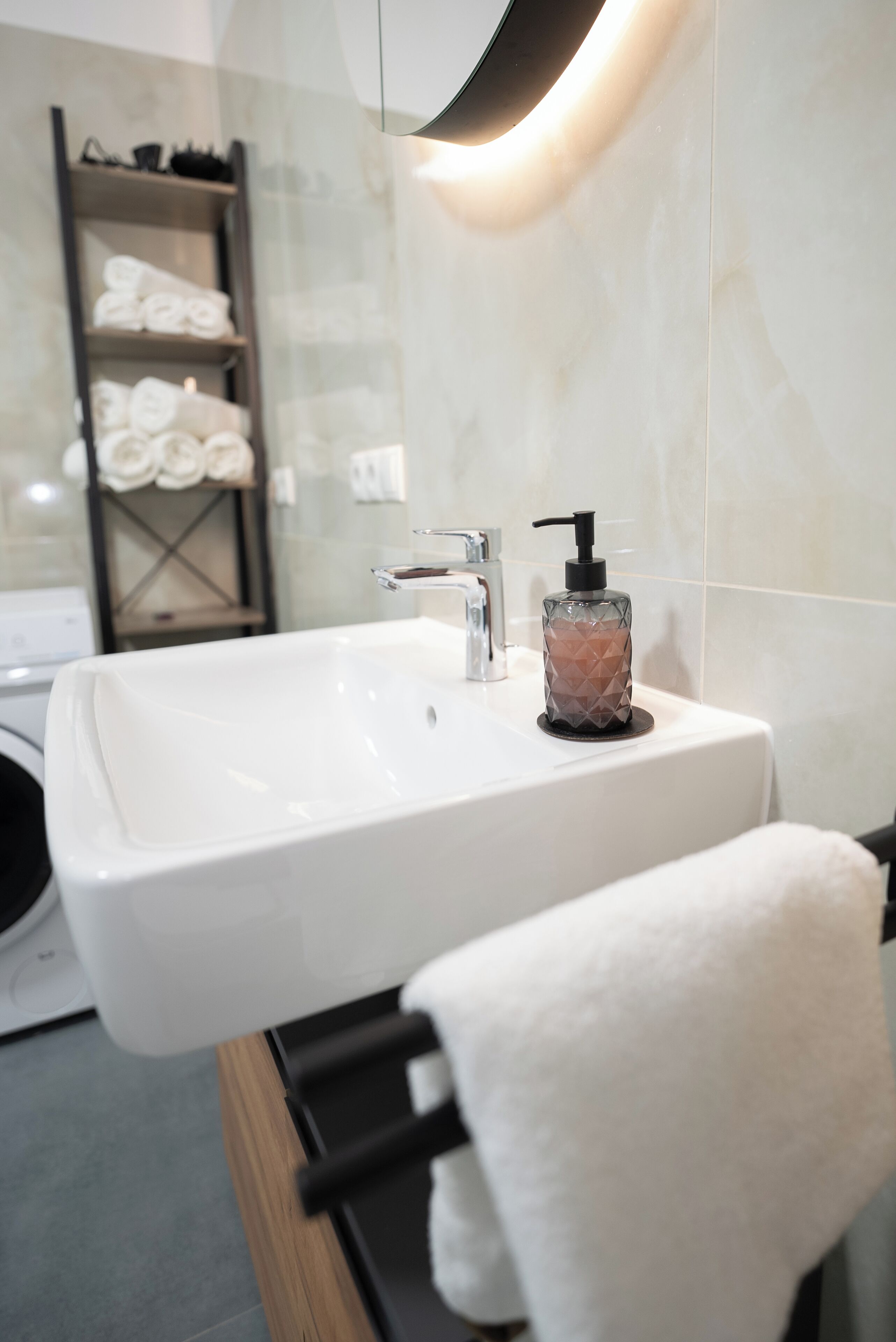 Ein modernes Badezimmer mit einem weißen Waschbecken, einem Seifenspender aus Glas und einem Handtuchhalter.