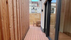 Pequeno deck de madeira com um banco e porta de vidro que dá para uma varanda.