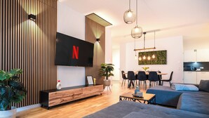 Sala de estar moderna com televisão de tela plana, área de jantar e cozinha ao fundo.