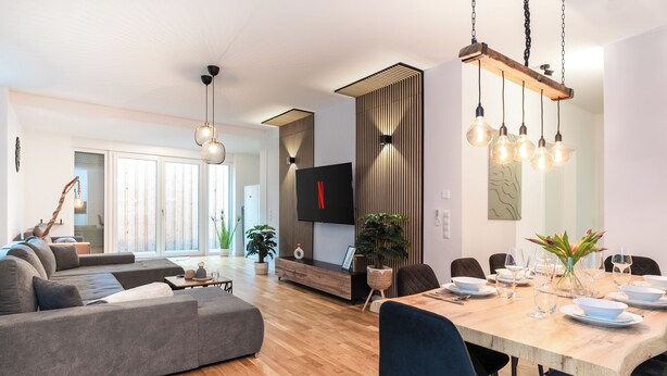 Uma sala de estar moderna com um sofá grande, mesa de jantar para seis pessoas e uma TV fixada na parede.