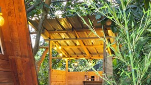 Un espace cuisine extérieur en bois, équipé d’une cuisinière à gaz, d’un distributeur d’eau et d’une étagère contenant des ustensiles de cuisine.