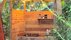 Une cuisine extérieure en bois, équipée d’une cuisinière à gaz, d’un distributeur d’eau et de luminaires suspendus.