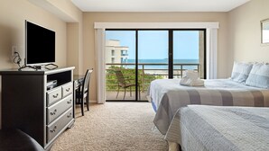 Habitación de hotel con una cama grande, televisión, escritorio con silla y balcón con vista al océano.