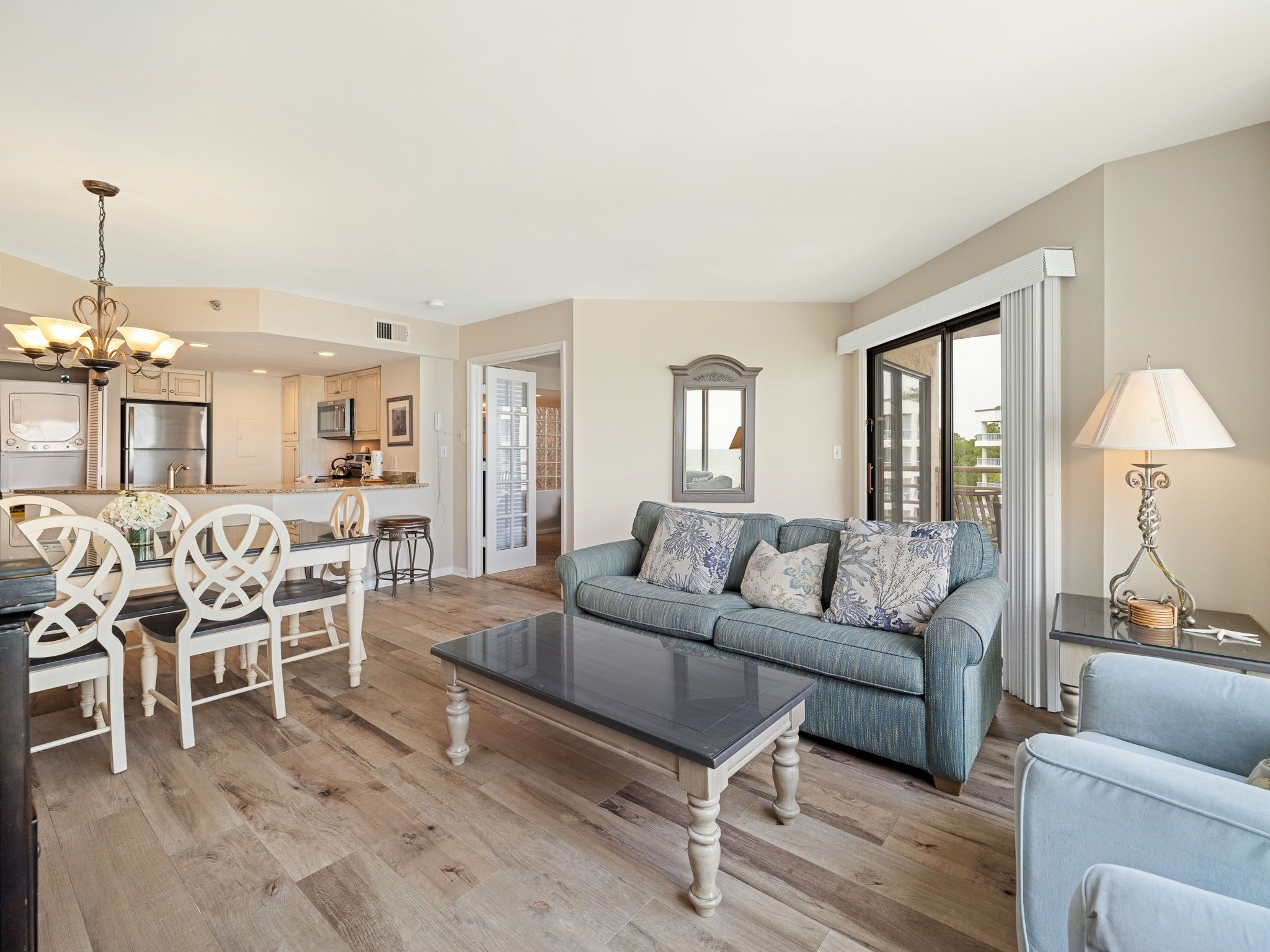 A spacious living area with a sofa, coffee table, and dining set. A kitchen is visible in the background.
