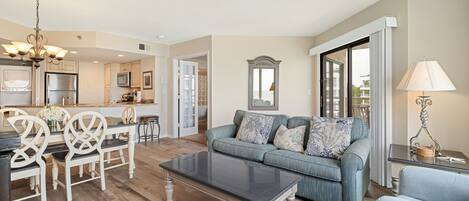A spacious living area with a sofa, coffee table, and dining set. A kitchen is visible in the background.