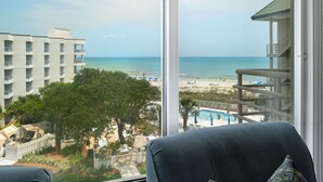 Vista desde un balcón hacia una playa, con una piscina y un edificio al fondo.