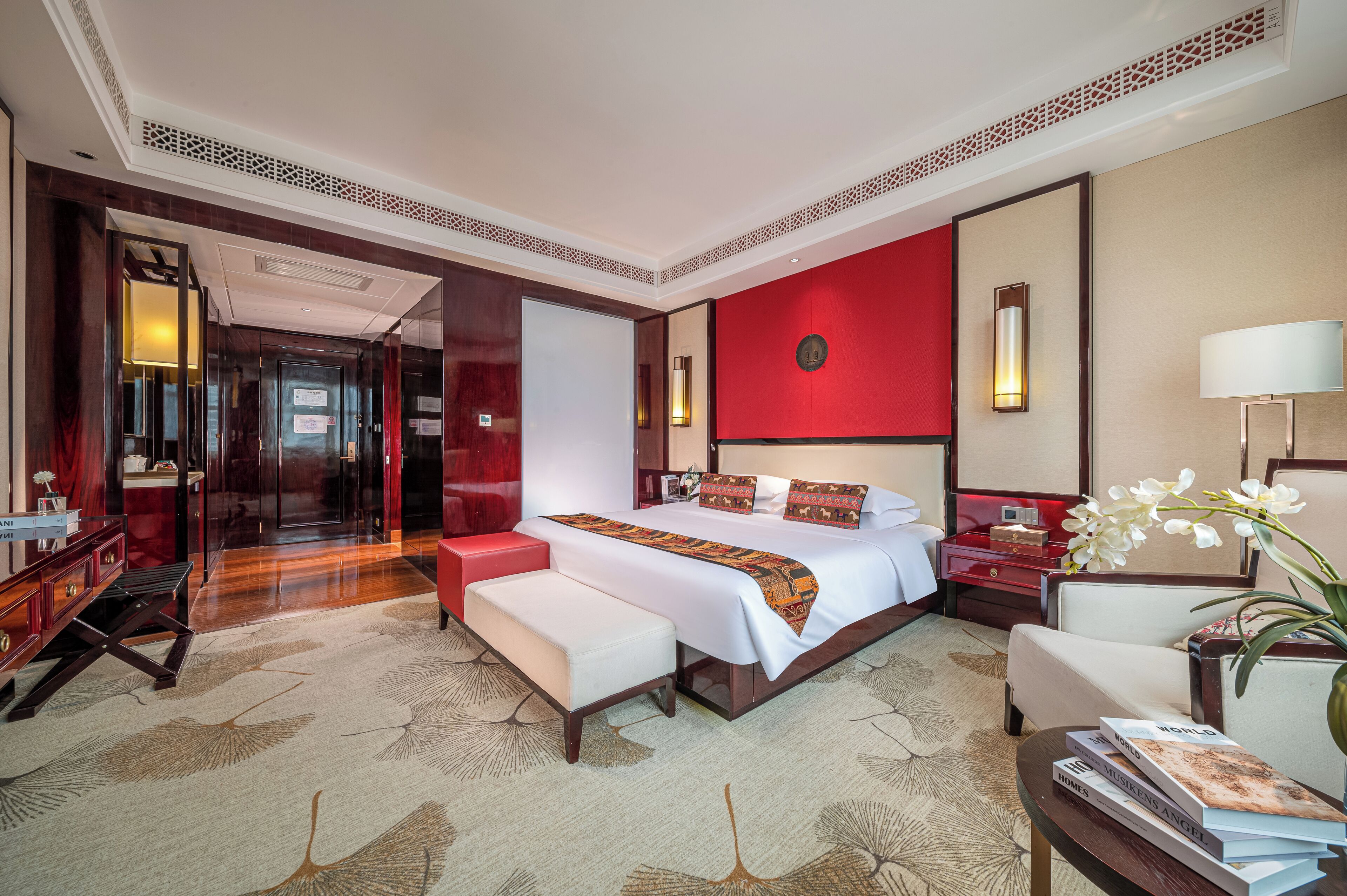 A hotel room with a large bed, a desk, a chair, a nightstand, and a red accent wall.