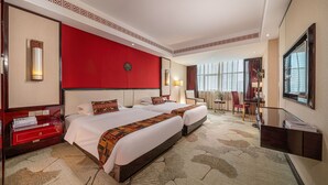 A hotel room with two beds, a red accent wall, a large window, and a reception desk.