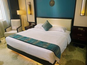 A hotel room with a large bed, a chair, a nightstand, and a wall clock.