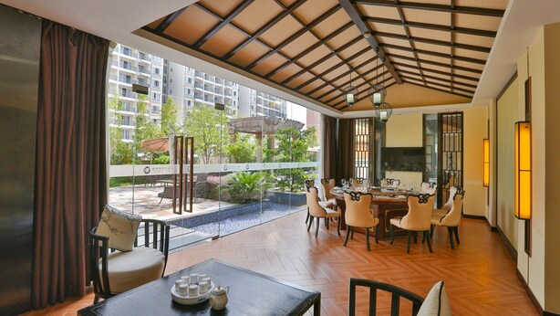 A modern dining area with a wooden table and chairs, large windows offering a view of the cityscape, and a ceiling with a grid pattern.