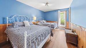 Ein Schlafzimmer mit zwei Betten, einem Deckenventilator, einem Fenster mit Vorhängen und einem kleinen Nachttisch.