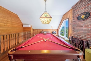 A pool table with a red felt surface, wooden railings, and a hanging light fixture.