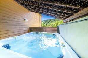 Un bain à remous avec une terrasse en bois et une vue sur une colline boisée.