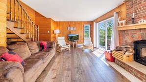 Ein Holzinnenraum mit einer Couch, Sesseln, einem Kamin und einem Fernseher.