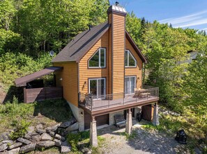 Une cabane en bois dotée d’un balcon, de fondations en pierre et d’une cheminée.