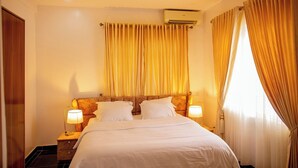 Une chambre d’hôtel avec un lit, deux lampes de chevet, une fenêtre avec des rideaux et un appareil de climatisation.