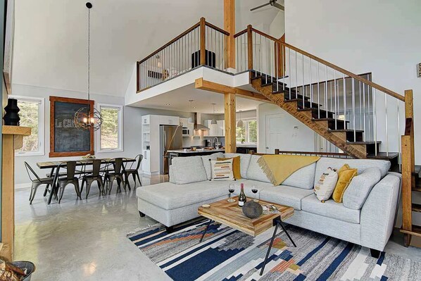 A spacious living area with a large sofa, a wooden coffee table, and a staircase leading to an upper level. - Spa & Game Room | Le Chic Rustique (Saint-Côme)
