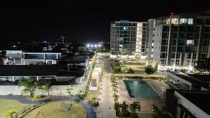 A nighttime view of a hotel with a swimming pool, a tennis court, and a parking area.