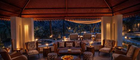 A covered outdoor seating area with chairs and tables, a decorative ceiling, and a view of the outdoors.