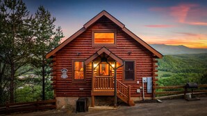 A log cabin with a porch, a small staircase, and a view of the surrounding landscape.