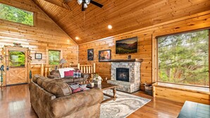 A log cabin interior with a stone fireplace, wooden walls, and a cozy seating area.