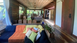 A spacious room with a wooden ceiling, a sofa with cushions, a dining table, and a refrigerator. - Sítio São Pedro da Serra (Nova Friburgo)