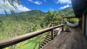 A wooden deck with a hammock, overlooking a lush green landscape and mountains. - Sítio São Pedro da Serra (Nova Friburgo)