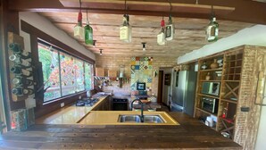 A kitchen with a central island, bar stools, hanging bottles, and a brick wall backsplash. - Sítio São Pedro da Serra (Nova Friburgo)