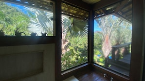 A bathroom with a bathtub, wooden floor, and large windows offering views of tropical foliage. - Sítio São Pedro da Serra (Nova Friburgo)