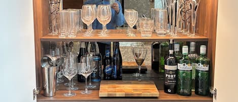 A bar area with shelves of liquor bottles, glasses, and a wooden countertop.