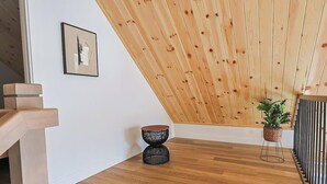 A modern interior with a wooden sloped ceiling, a staircase, a small round black table, and a potted plant.