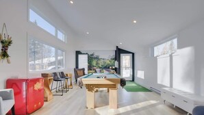 A modern room with a pool table, a red cabinet, and large windows.