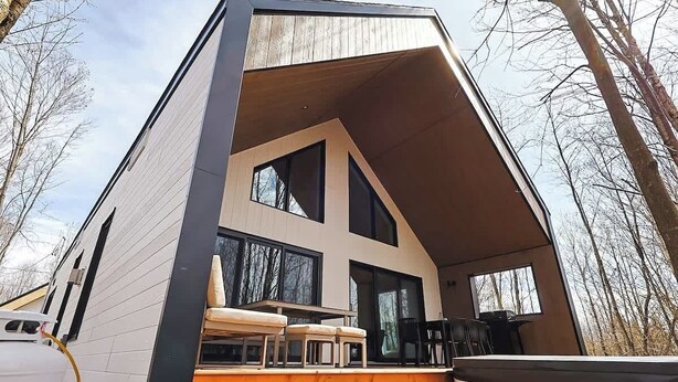 A modern cabin with a sloped roof, large windows, and a deck area with seating.
