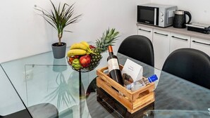 A glass table with a fruit bowl, a bottle, and a wooden crate with a bottle and a card. - Sunny Nest Apartment 2 in Ixia (Ialisos)